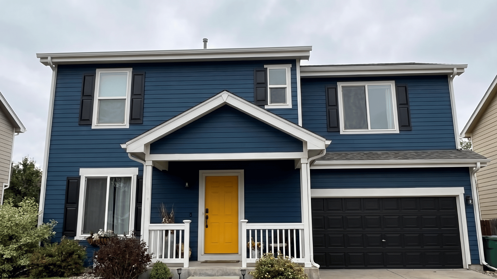 Two-story blue house exterior with white trim, black shutters, a black garage door, and a bright yellow front door.