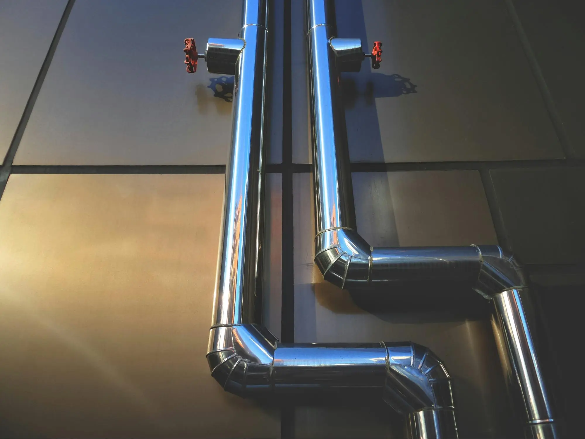 Stainless steel pipes with red valves on dark industrial wall