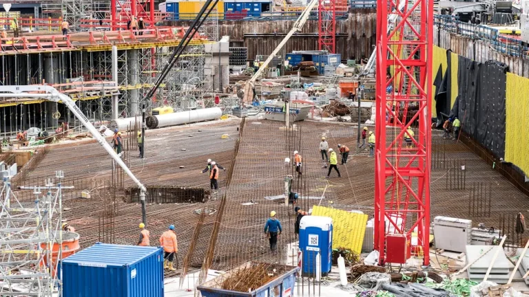 Construction site with workers and red cranes, rebar framework, and scaffolding in an urban setting