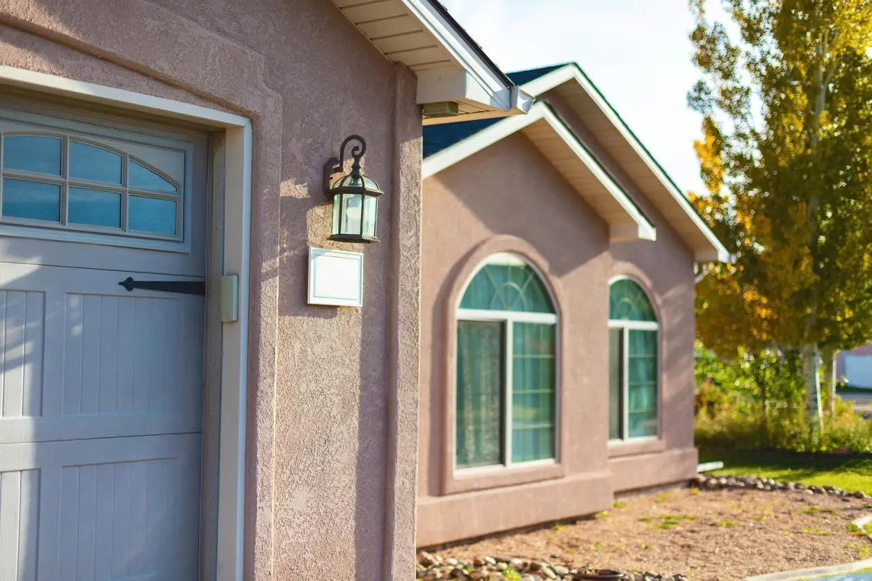 Stucco house exterior with arched windows, garage door, and exterior light under sunny skies