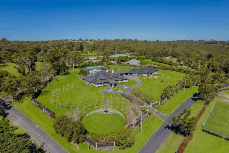 Large estate with solar panels surrounded by lush greenery and extensive landscaping in a rural area