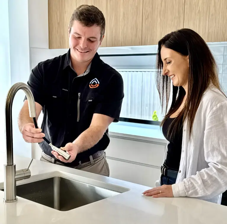 Man explaining kitchen faucet features to woman in modern kitchen setting