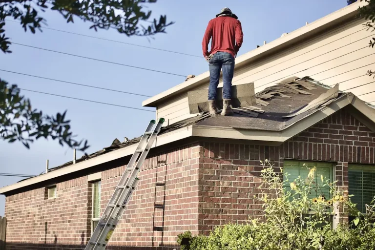 Worker standing on roof making repairs with ladder leaning against brick house