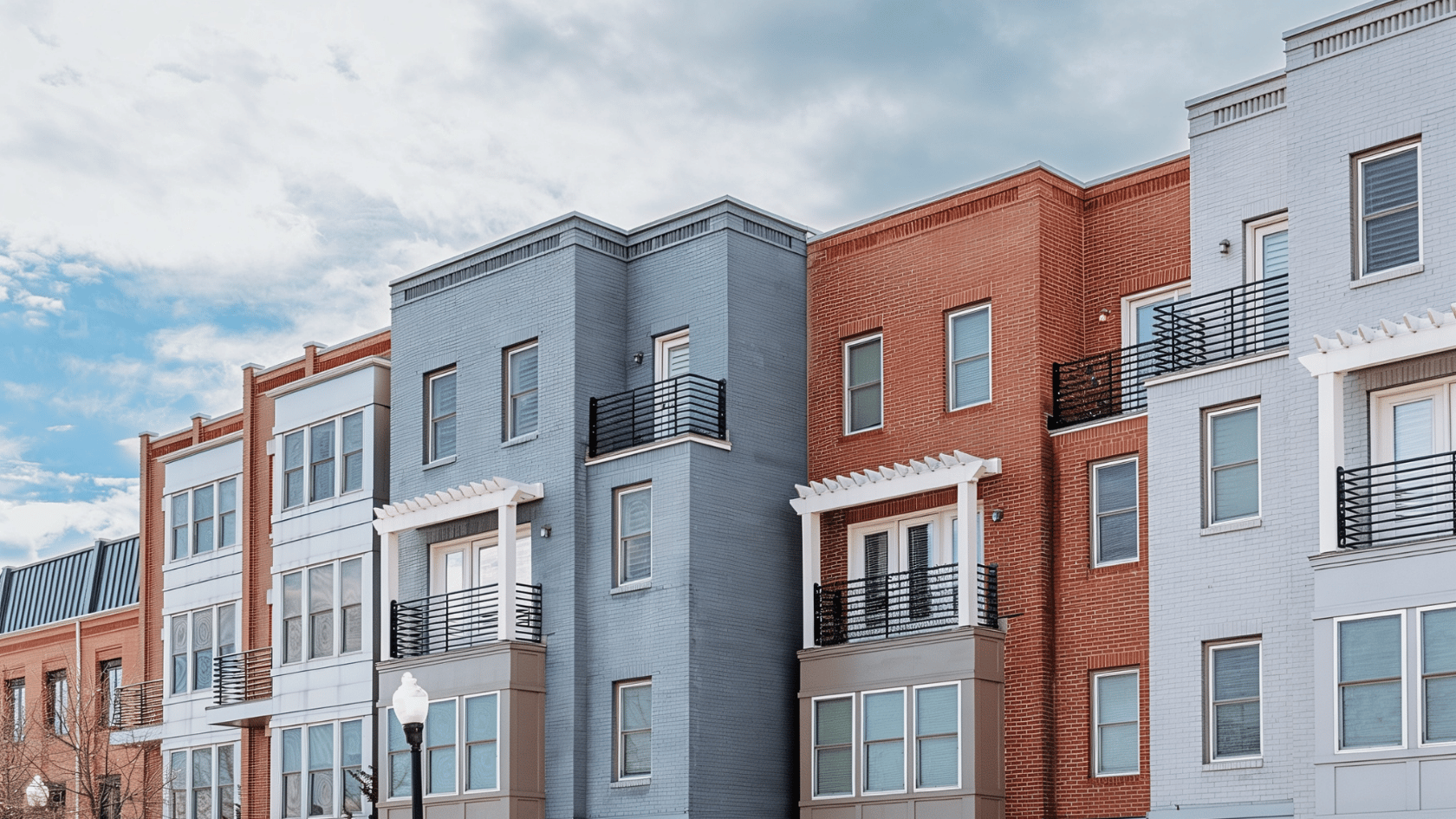 Row of modern buildings with brick and gray facades, balconies, and streetlamp under blue sky