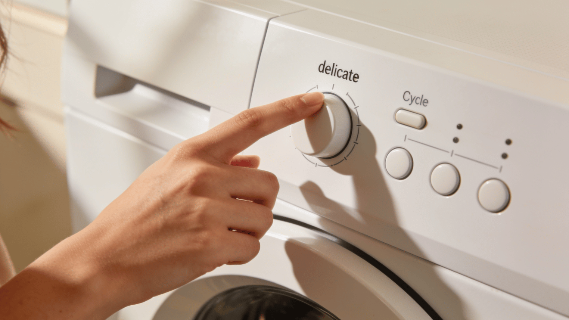 a hand carefully selecting the delicate gentle wash cycle on a modern white washing machine