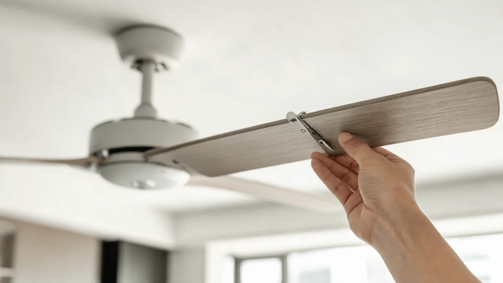 Hand holding balancing clip on ceiling fan blade while adjusting its position