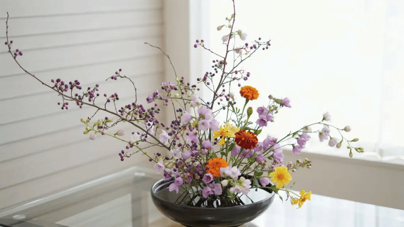 Floral arrangement with purple berries, yellow blooms, and delicate flowers in a black vase.