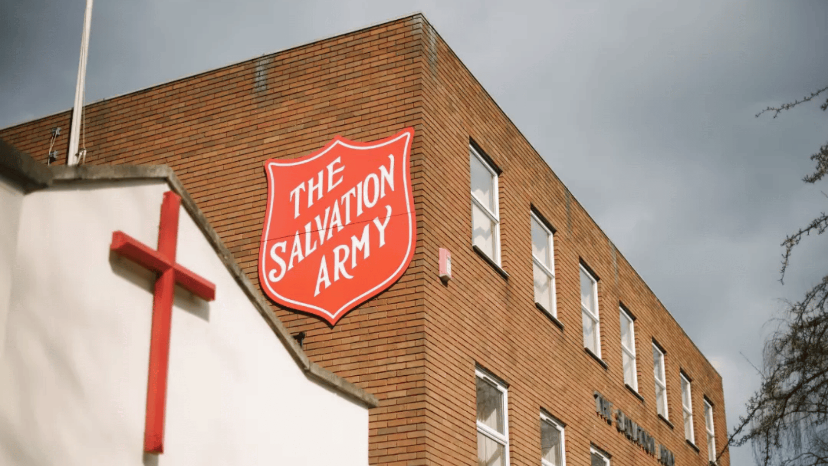 Brick building with “The Salvation Army” red shield sign and a cross on a nearby church.