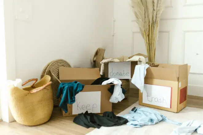 Cardboard boxes labeled keep, donate, and trash with clothes in a bright hallway setting