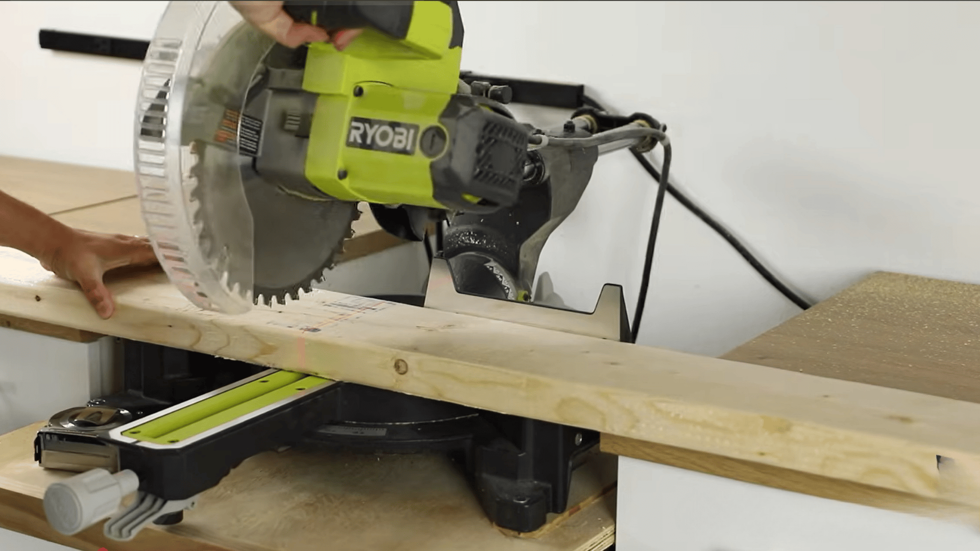 A miter saw cutting a long wooden board to size for a DIY woodworking project.
