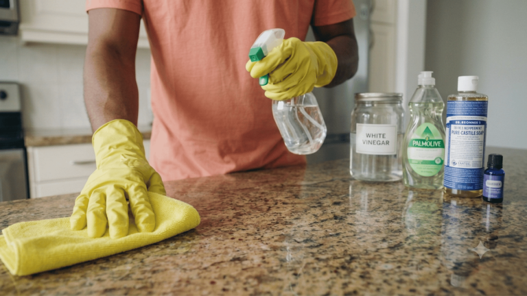 Wiping kitchen counter with a spray bottle next to diy all purpose cleaner ingredients.