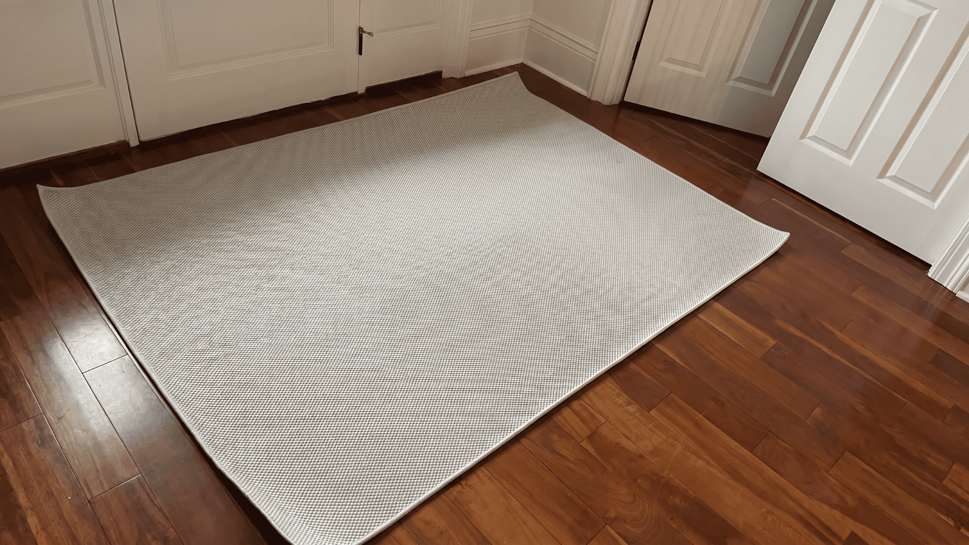 A white Ernesta rug with visibly curled and lifted edges laid on hardwood floors, a commonly reported issue among buyers.