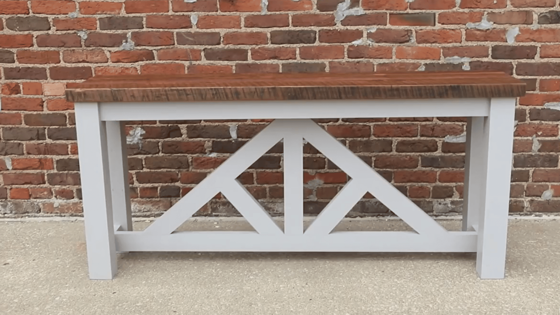 finished farmhouse console table with white frame and stained wooden top placed against a brick wall
