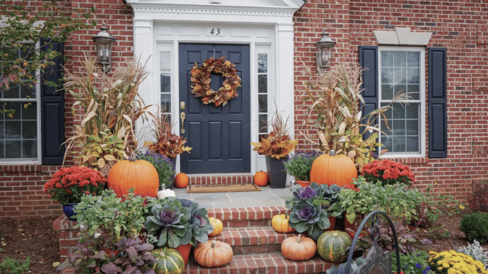 Matching fall containers with mums, ornamental grass, ivy, and pumpkins on both sides of a front door
