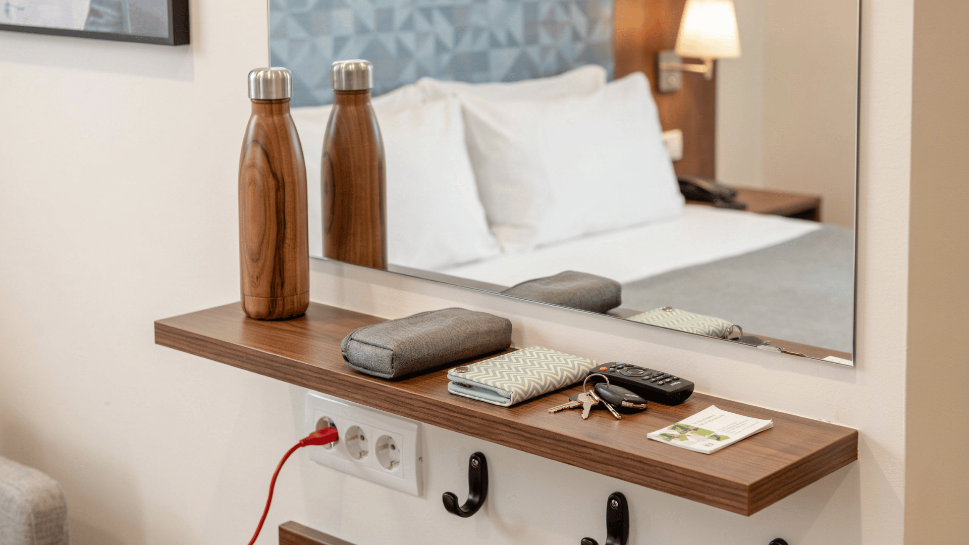 A wooden shelf in a guest room featuring a TV remote, keys, a wallet, and an outlet, highlighting tech access