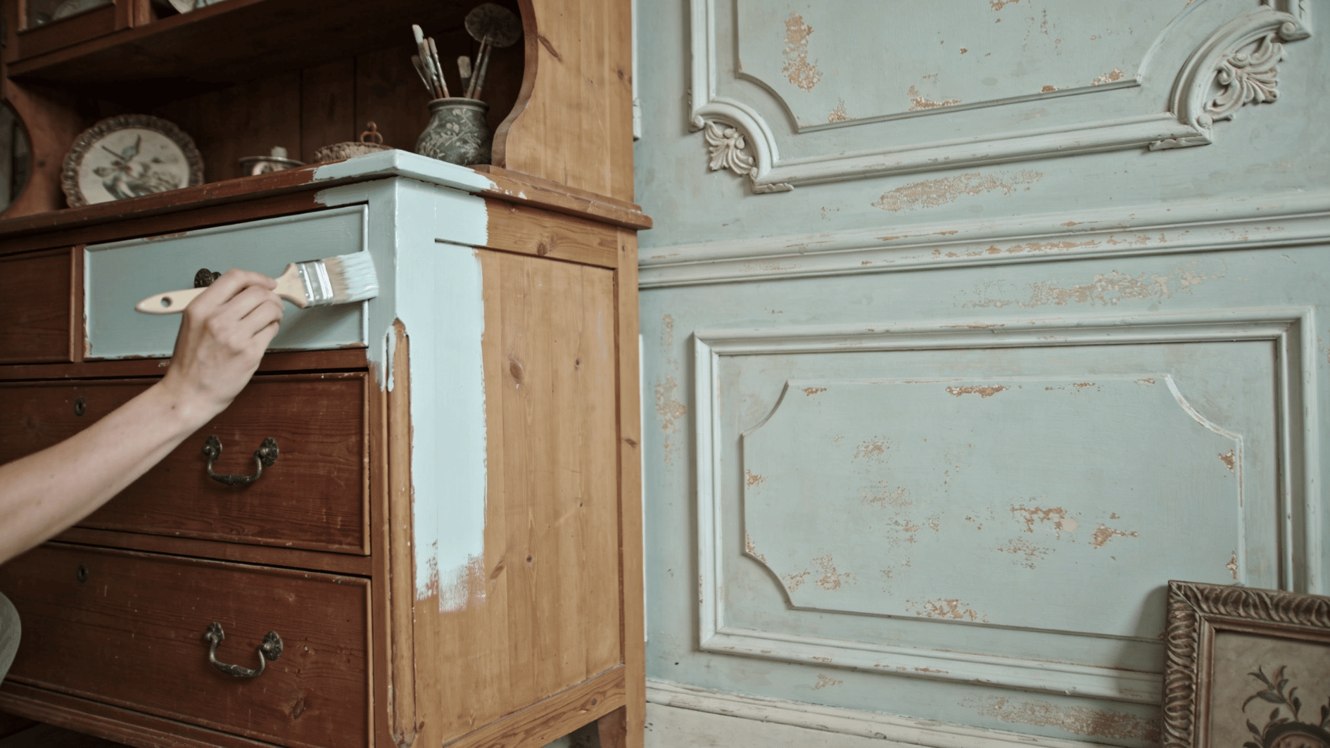 hand painting an antique wooden dresser drawer with milk paint beside a distressed blue cabinet