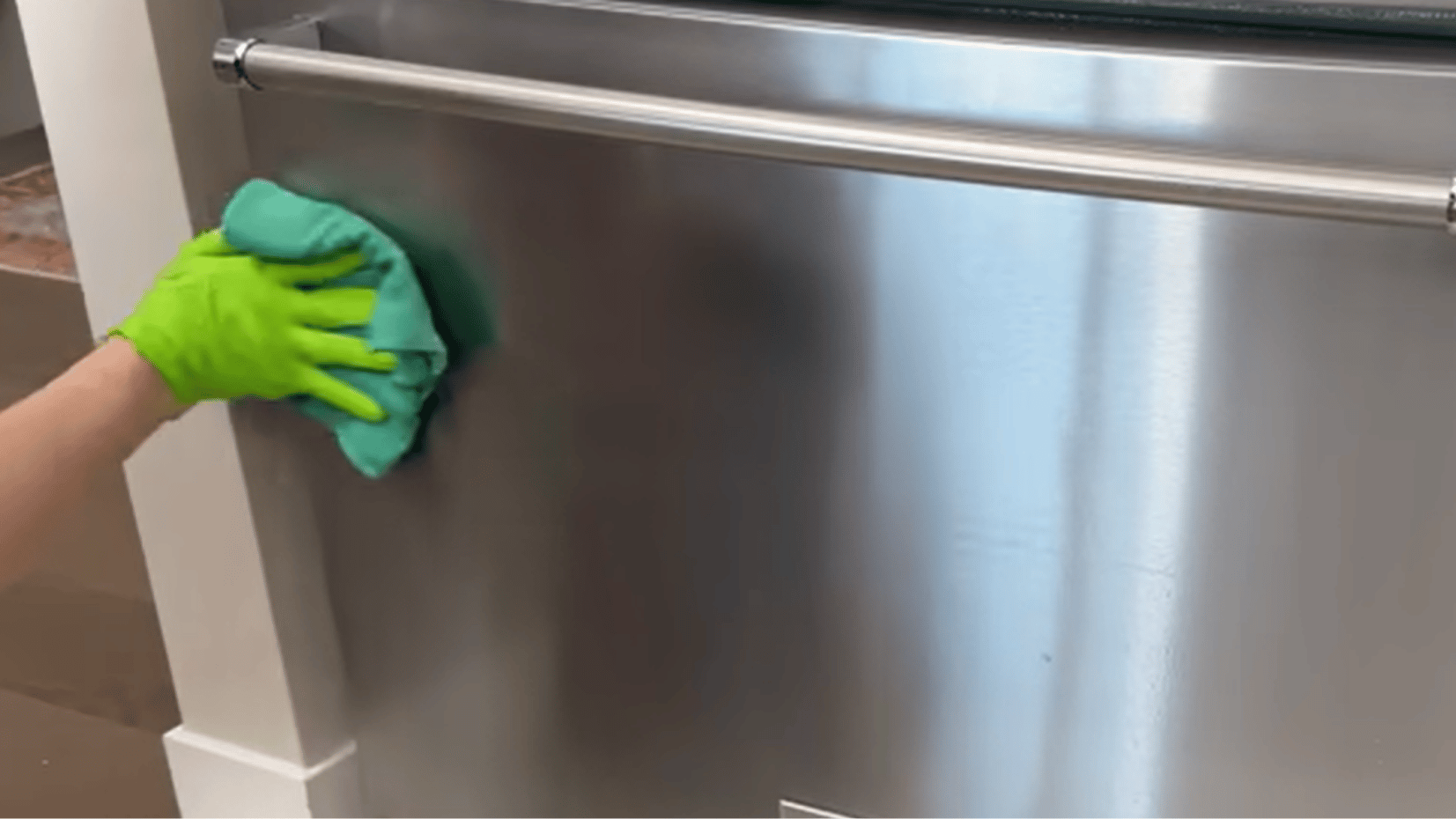 hand wiping stainless steel fridge door with a green cloth