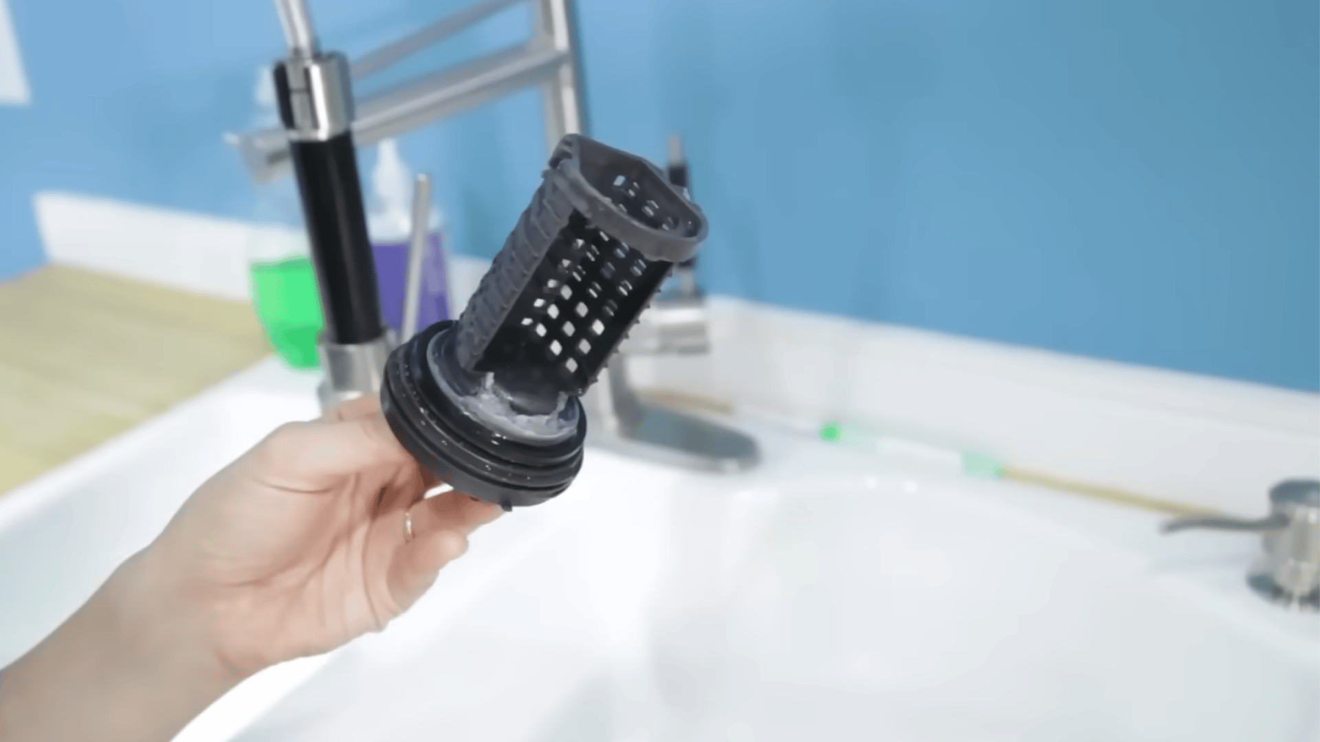 Holding up a dirty, removed washing machine drain pump filter to clean it