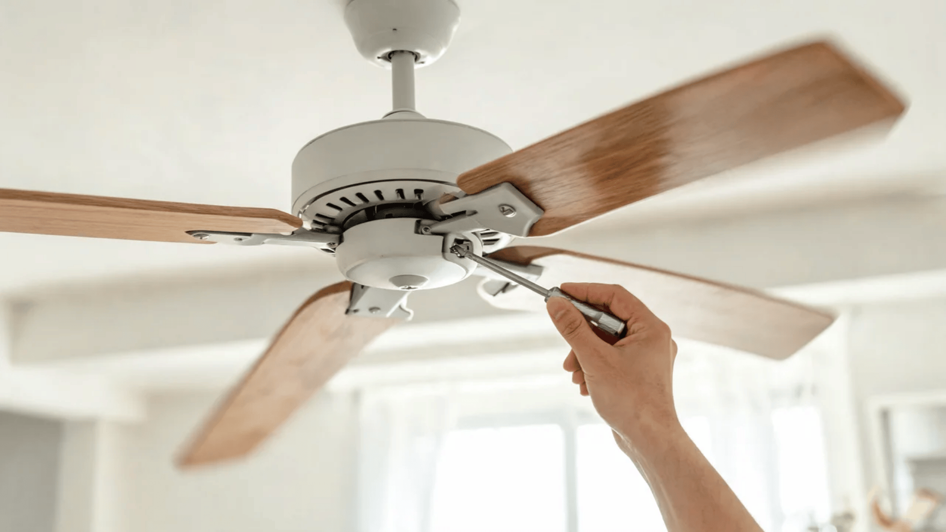 Hand tightening screw on ceiling fan blade bracket with screwdriver