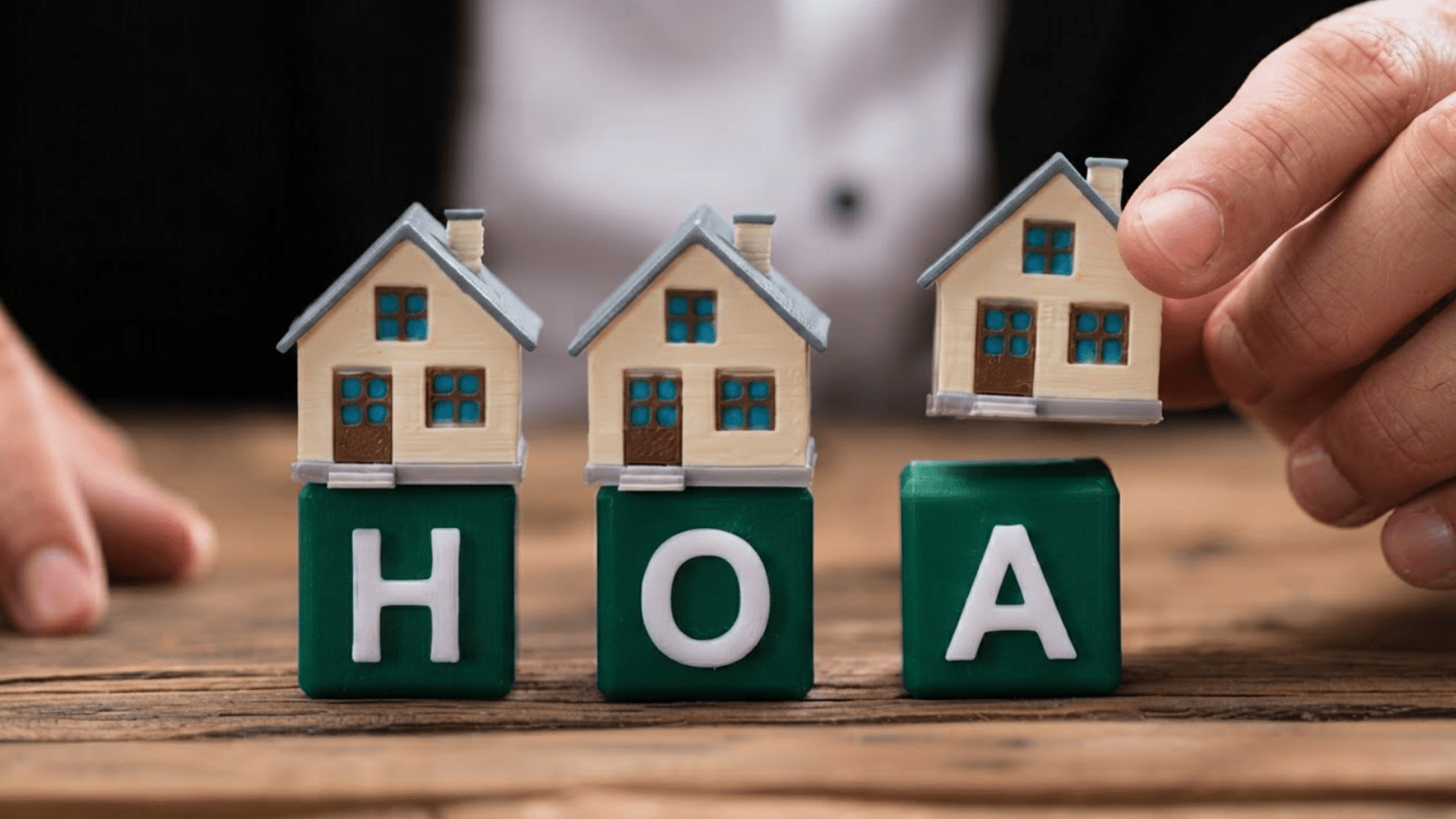 Hand placing miniature house on red blocks spelling HOA on wooden table