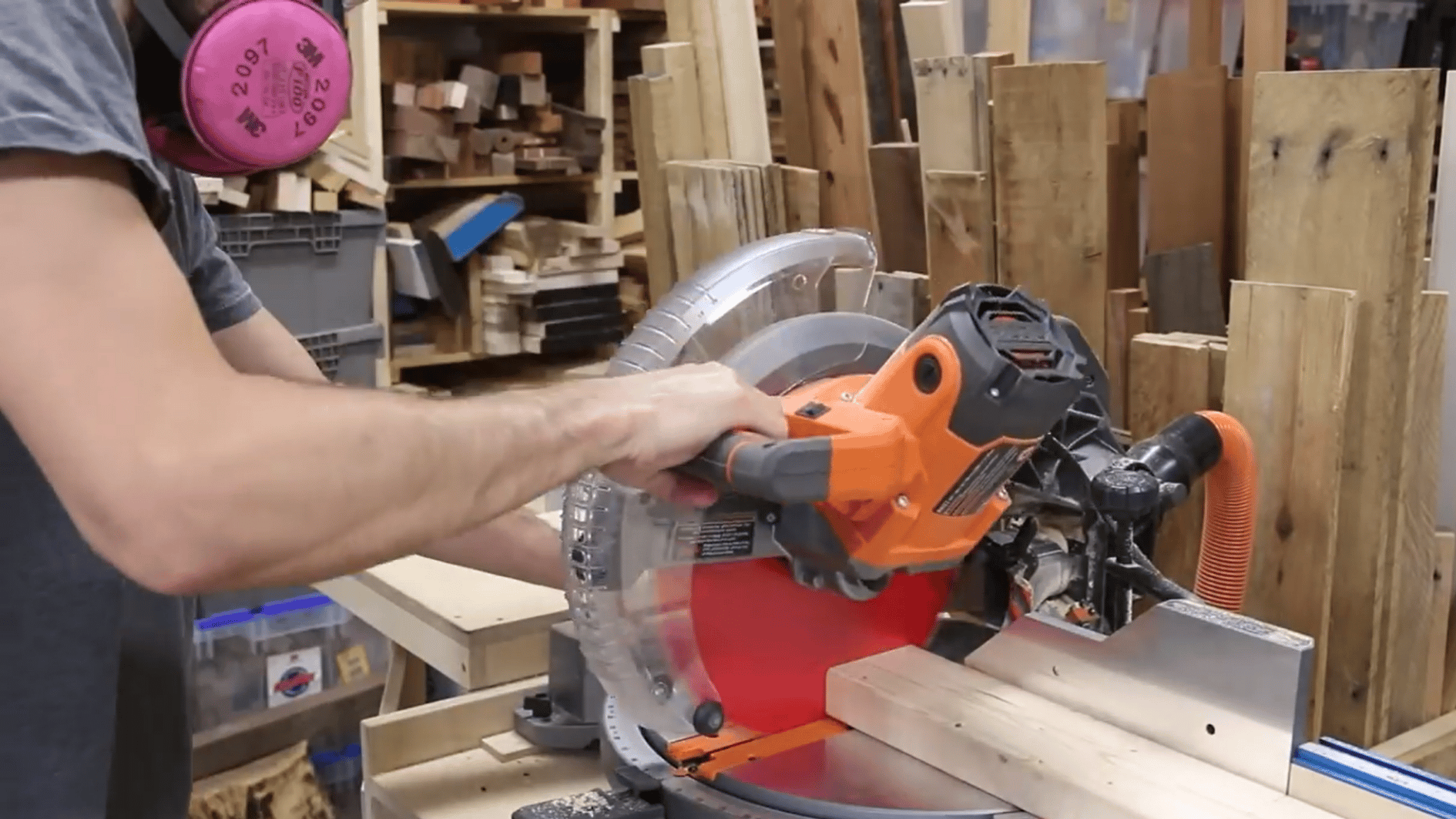 man cutting wooden boards with a miter saw inside a small home woodworking workshop with safety gear