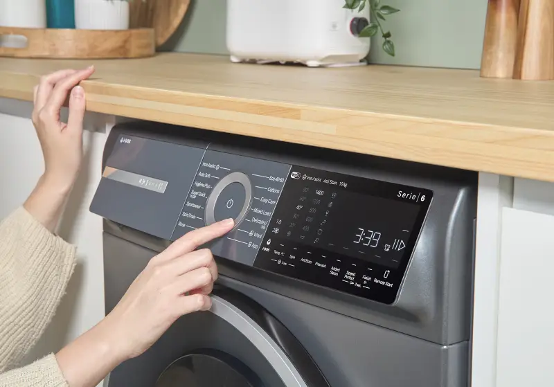 Person operating modern washing machine with digital display in a laundry room setting