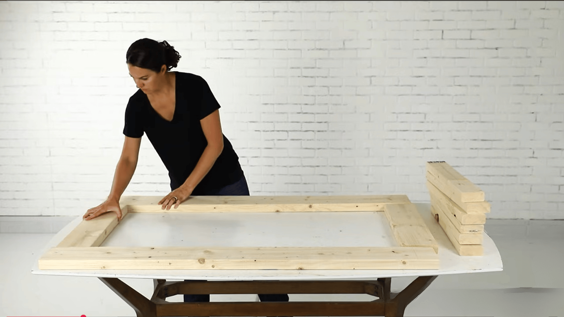 Person arranging wooden boards to measure and assemble a rectangular frame for a DIY woodworking project
