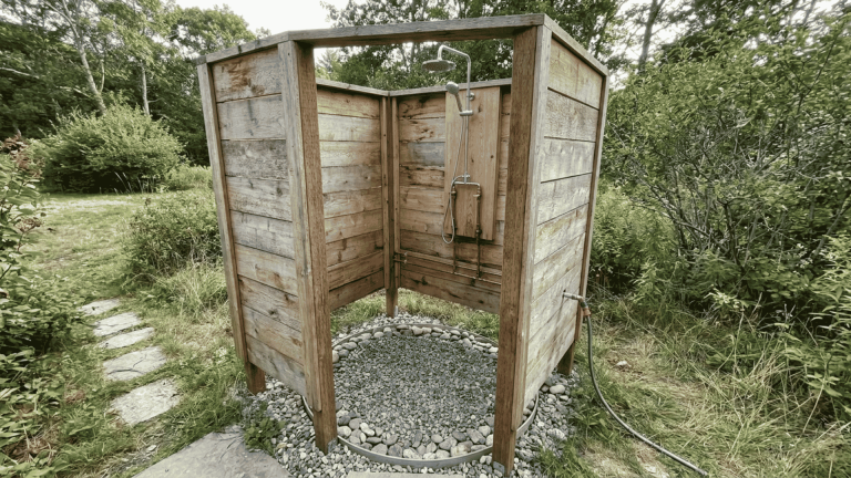 Outdoor shower ideas featuring a wooden enclosure with a gravel base and shower fixture in a backyard setting.