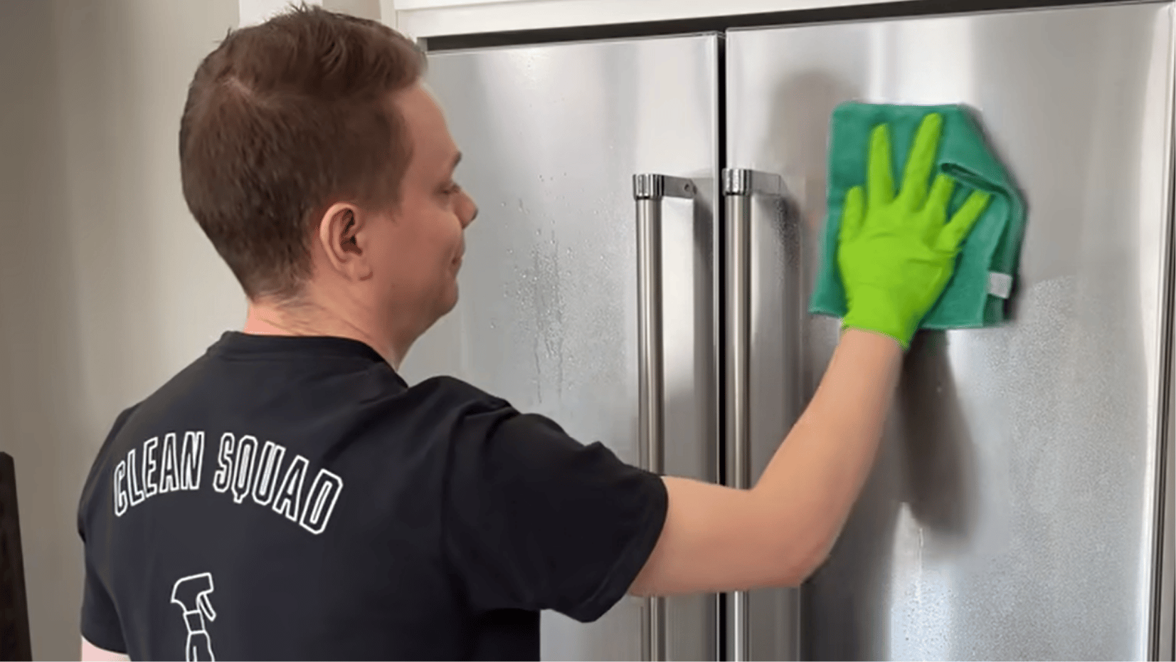 person wiping a stainless steel fridge with a microfibre cloth