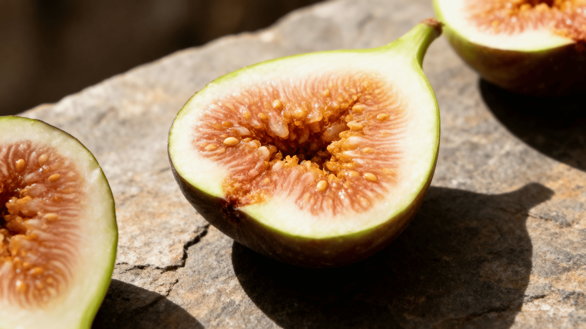 peter’s honey fig sliced on rustic stone showing green skin and amber pulp in natural light