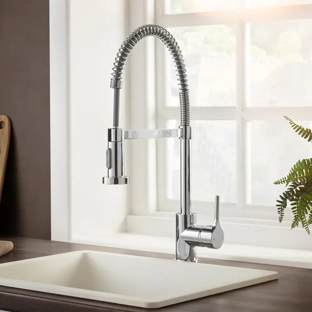 Stainless steel kitchen faucet with pull-down sprayer near white sink and window