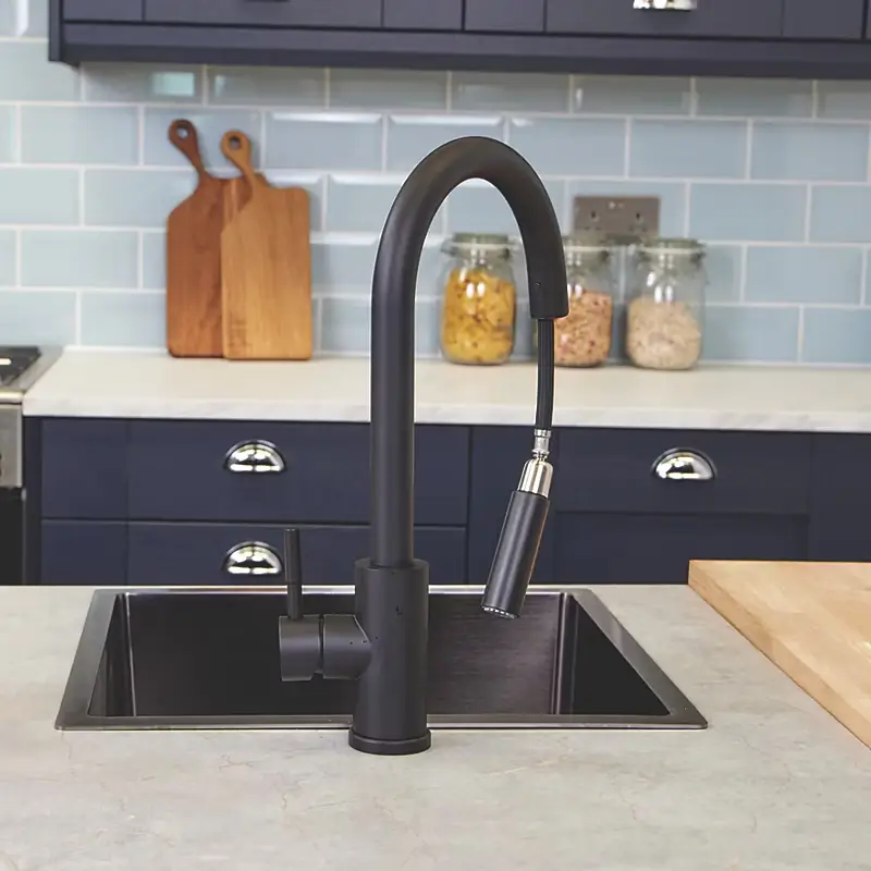 Matte black kitchen faucet over stainless steel sink in modern kitchen with light blue tile backsplash