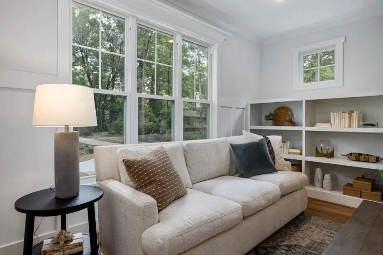 Modern living room with beige sofa and pillows near large windows and built-in white bookshelves