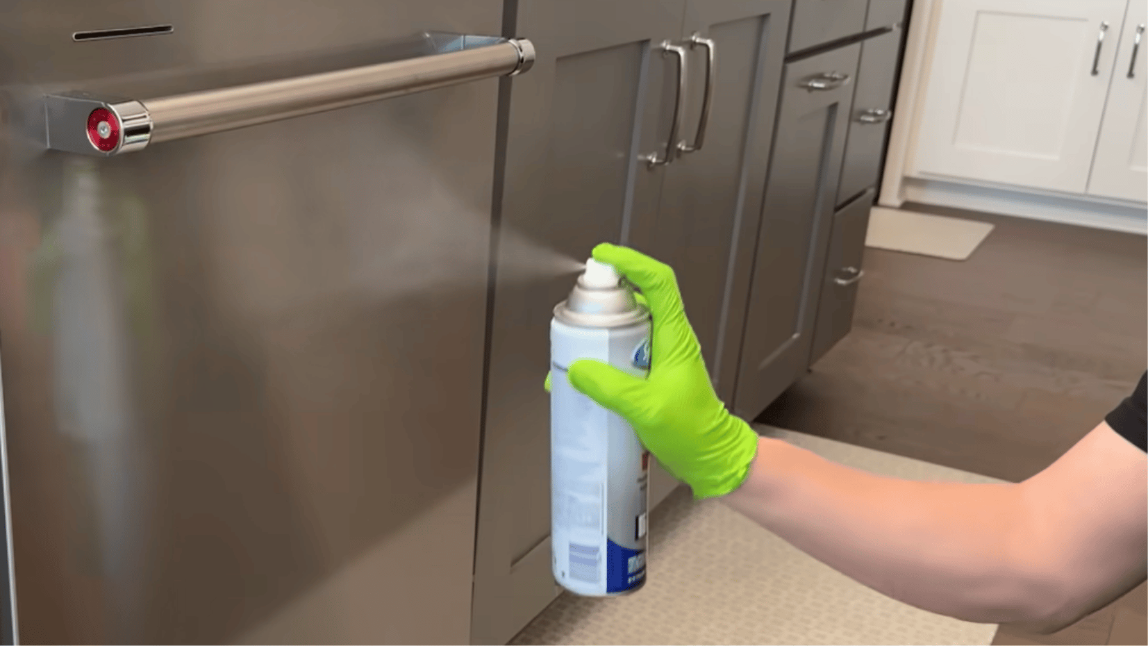 spraying cleaner onto a stainless steel fridge door with gloves