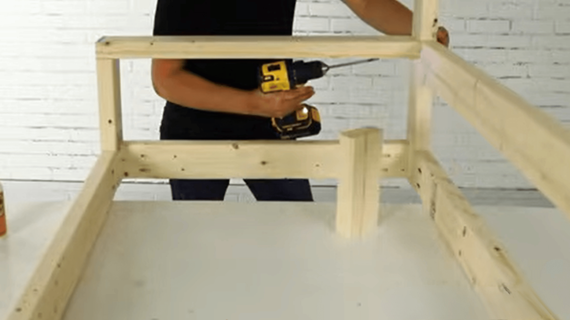 Person assembling a wooden porch swing frame using a drill on a work table.