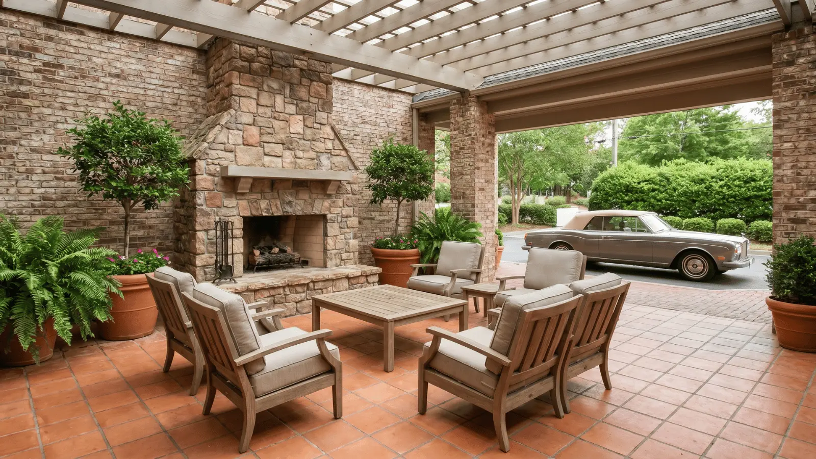 Outdoor senior living lounge with seating, fireplace, coffee table, plants, and a red classic car