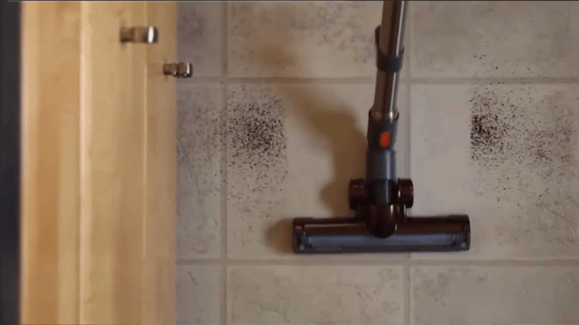 Black vacuum cleaner removing dirt from grout lines on a tiled bathroom floor.