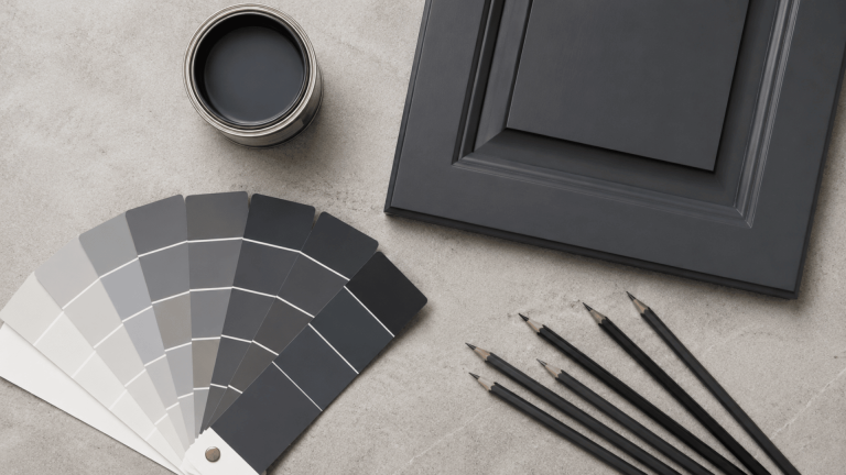Graphite paint swatches, dark cabinet sample, paint can, and pencils on a light gray surface