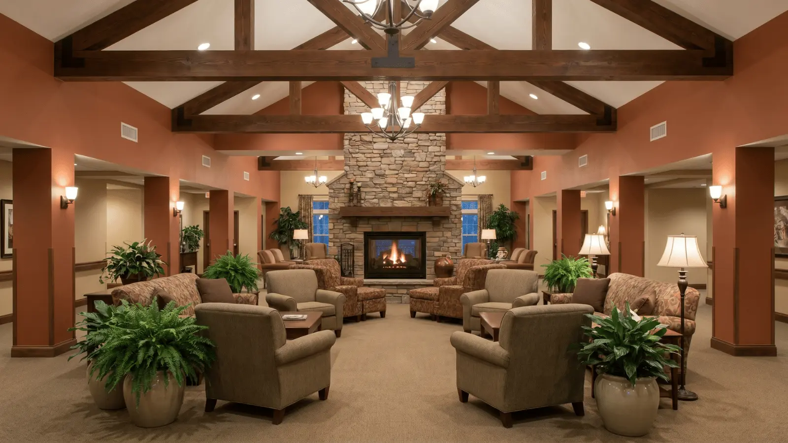 Senior living lounge with high ceilings, exposed beams, fireplace, upholstered seating, and plants