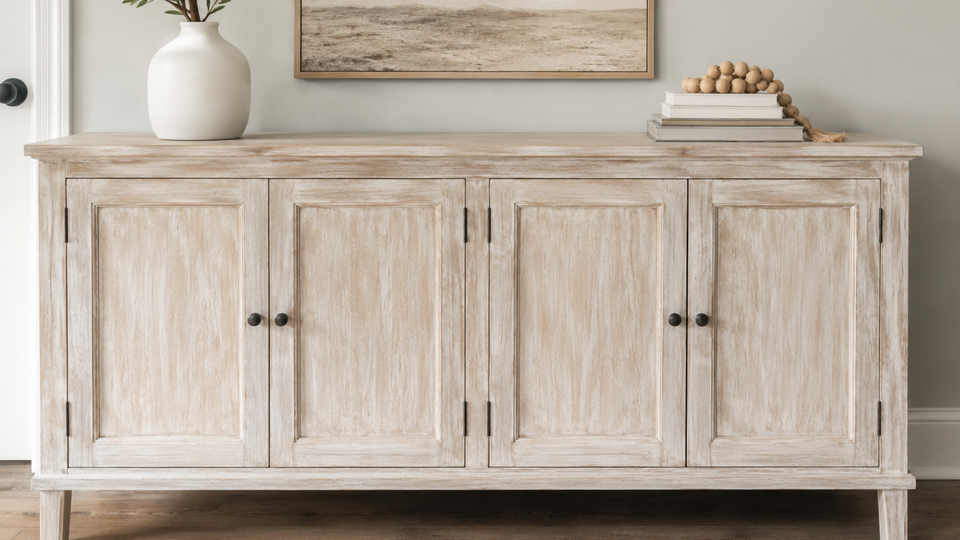 whitewashed wooden sideboard with black hardware styled with a vase books and neutral wall art above