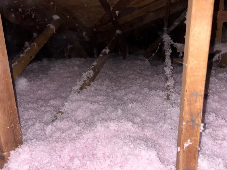 Wooden attic filled with pink insulation material under dim lighting