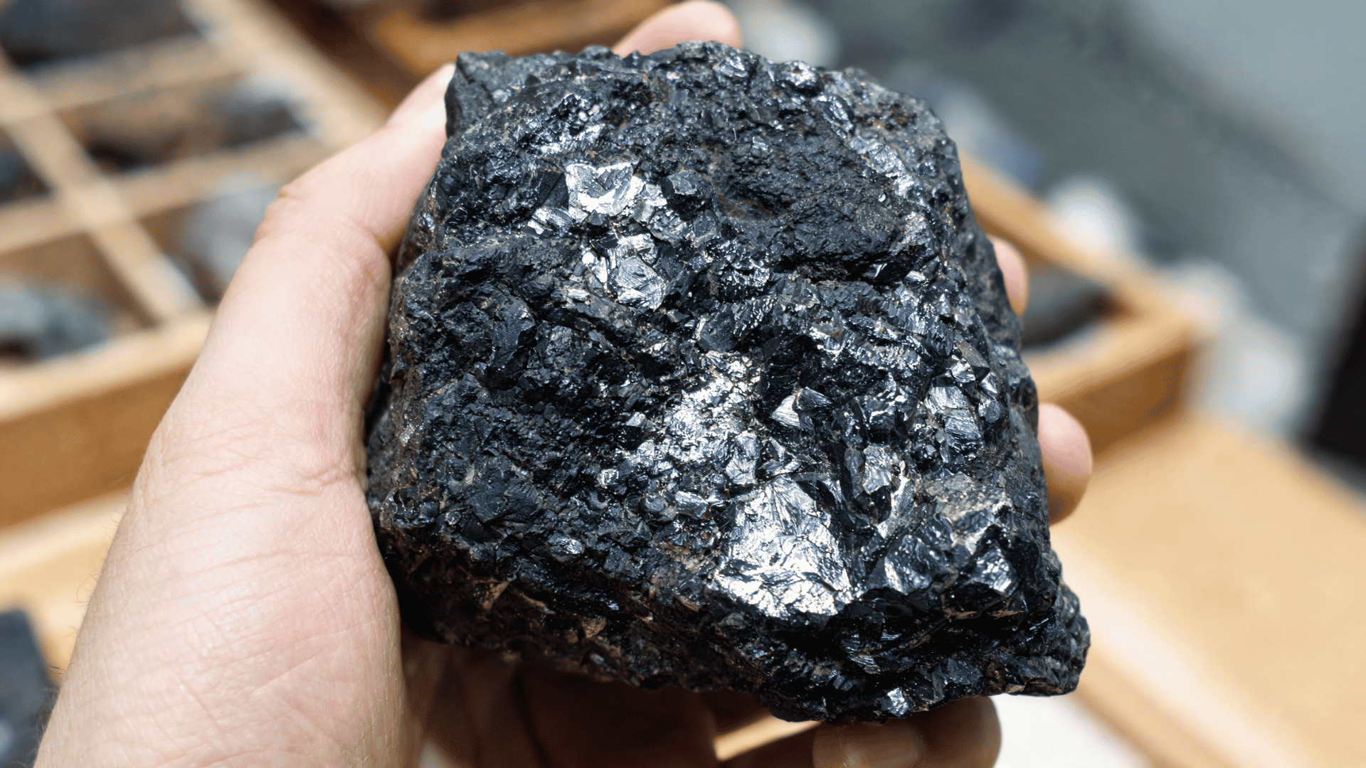Hand holding a rough black graphite rock with shiny metallic flakes and uneven texture in close-up view