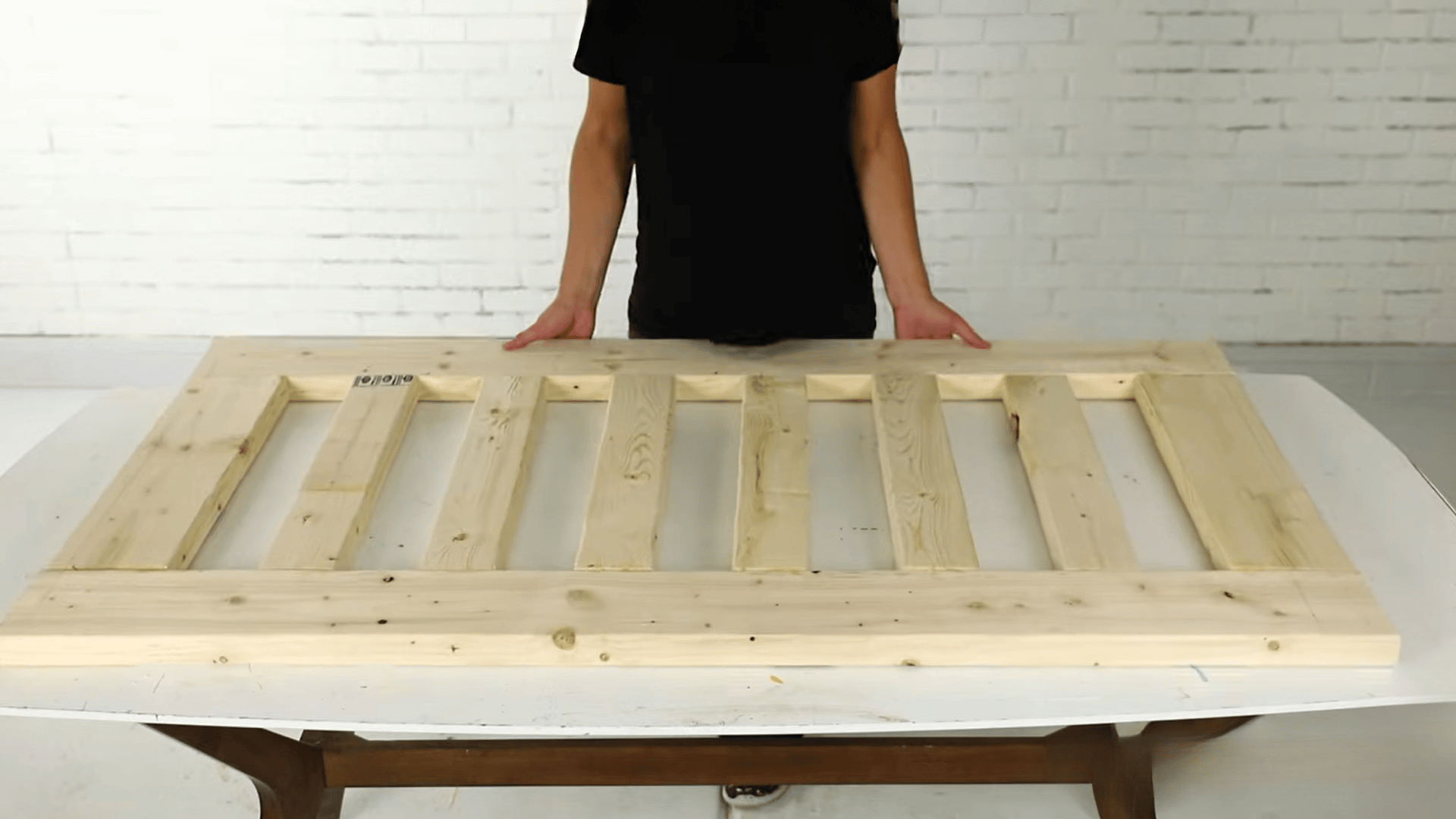 Person showing a partially assembled wooden porch swing frame on a work table.