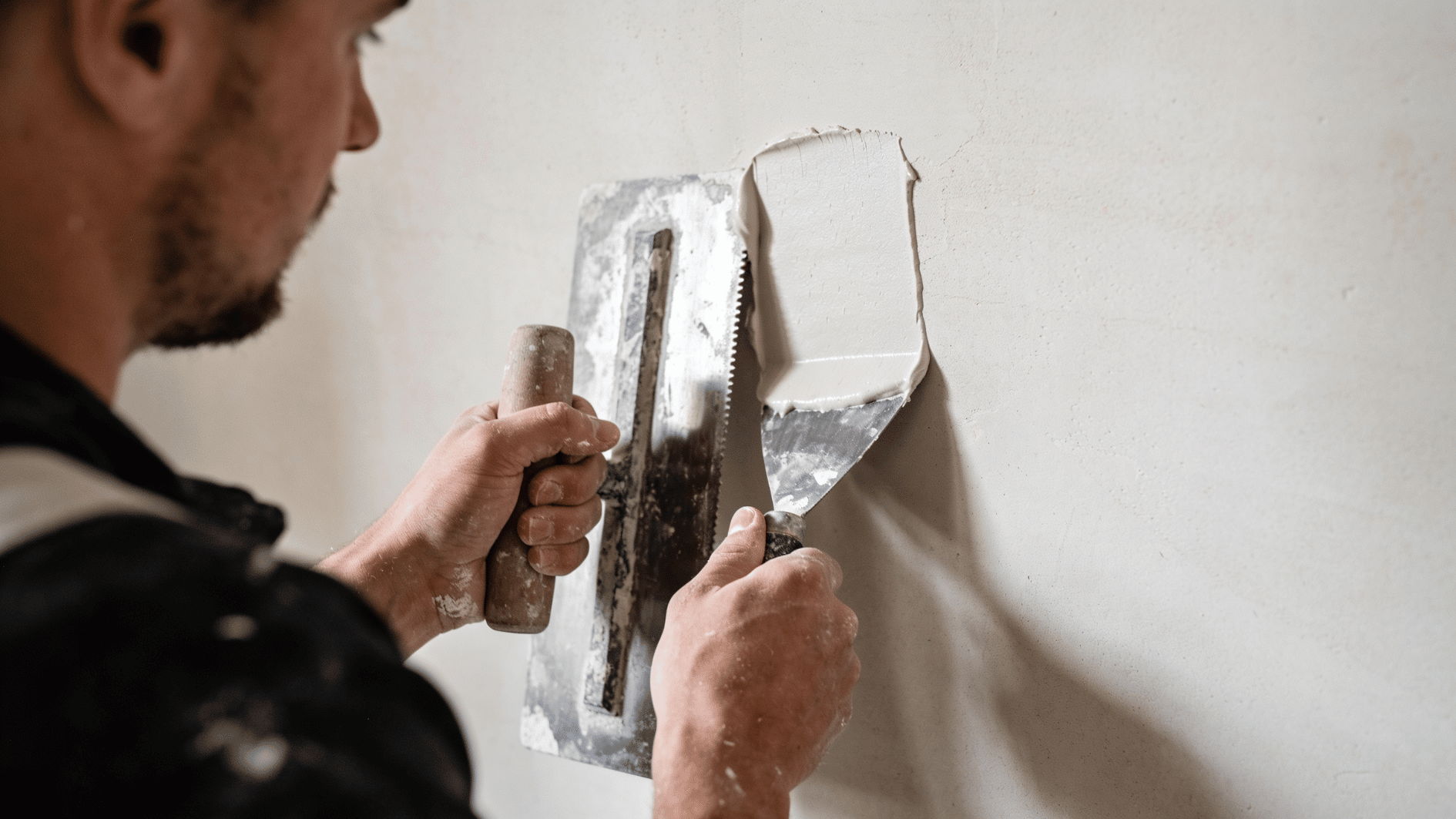 worker applying plaster to interior wall with trowel, smoothing patch around repair area (2)
