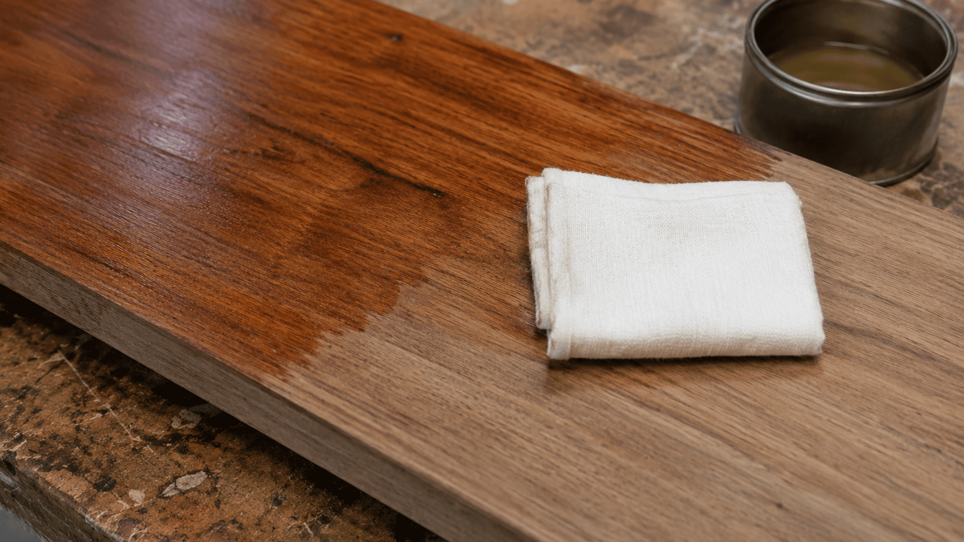 Wooden board with a cloth and finish container on a workbench during the wood finishing process.