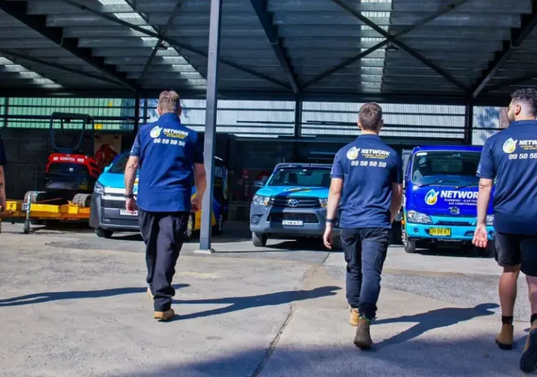Workers walking in industrial garage with branded fleet vehicles under metal roof structure