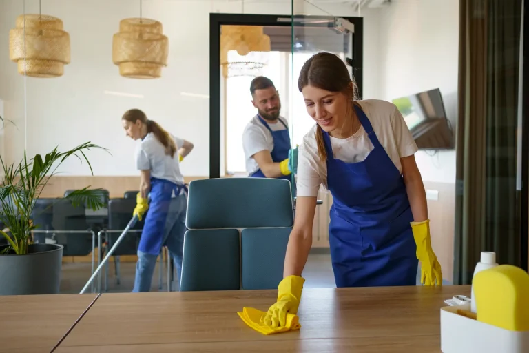 Cleaning staff in blue aprons tidying a modern office with yellow gloves