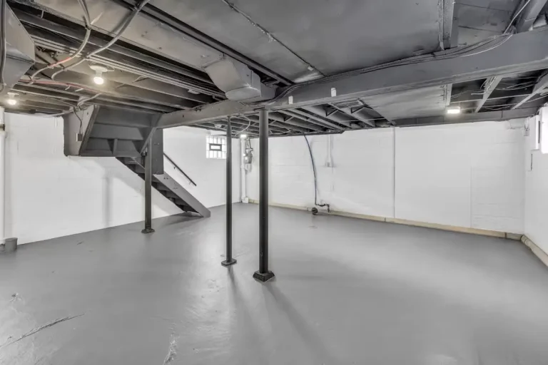 Unfinished basement with exposed beams and metal support columns in a neutral-toned setting