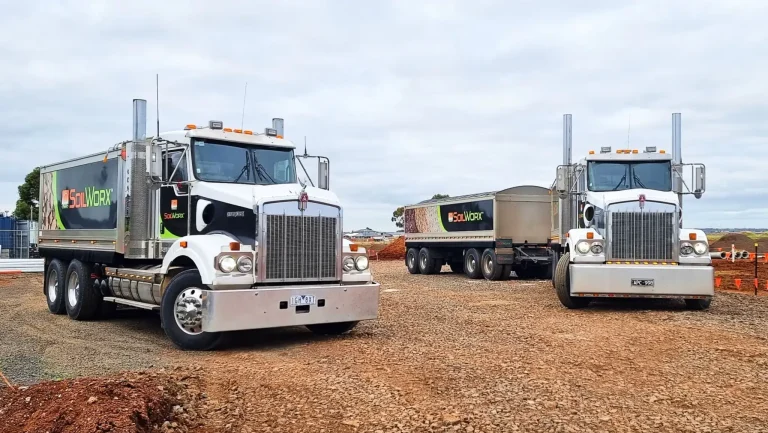 Two large trucks on a gravel construction site under cloudy skies
