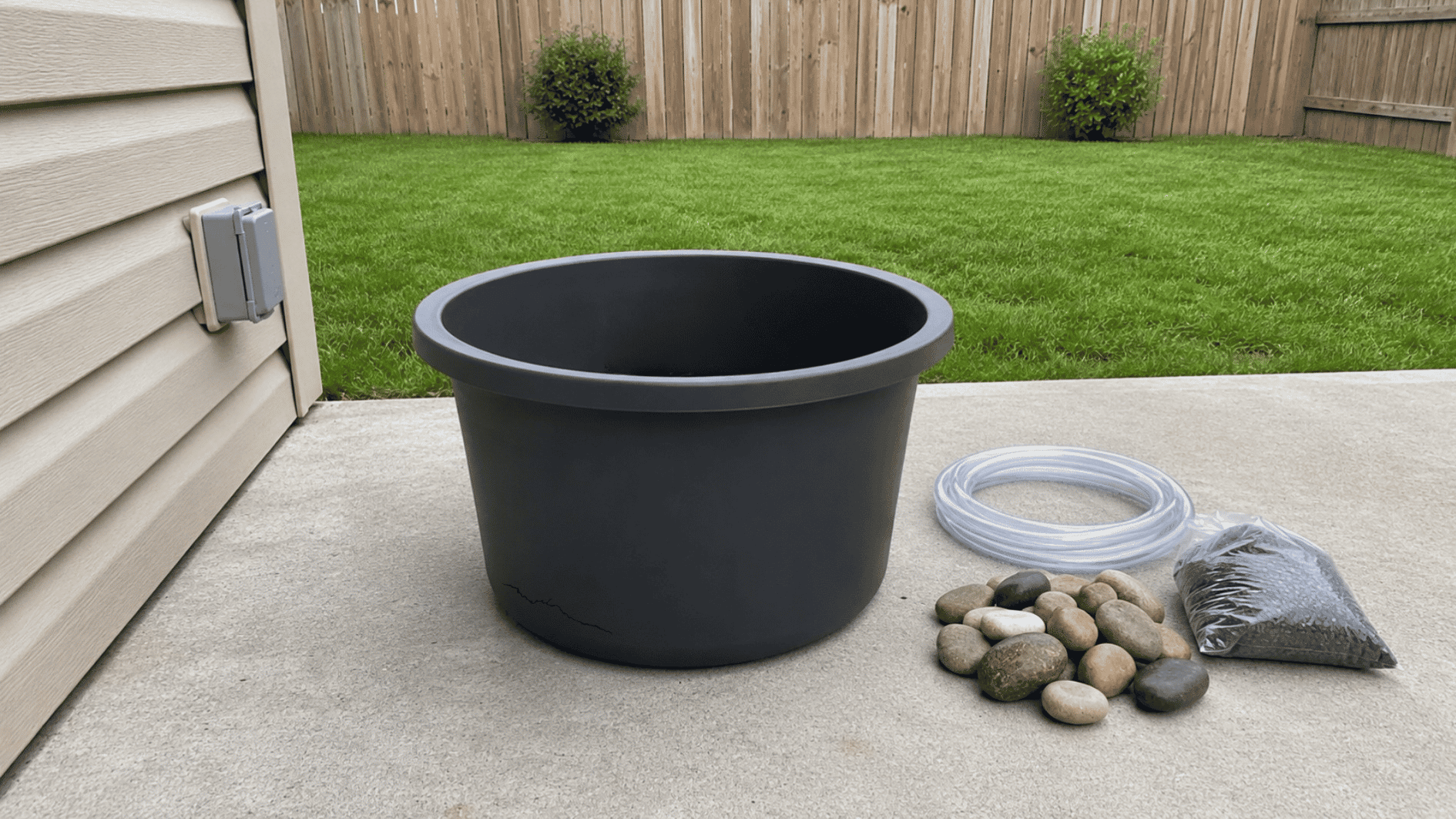 black tub with pump inside, next to tubing, stones, and gravel on backyard patio (1)